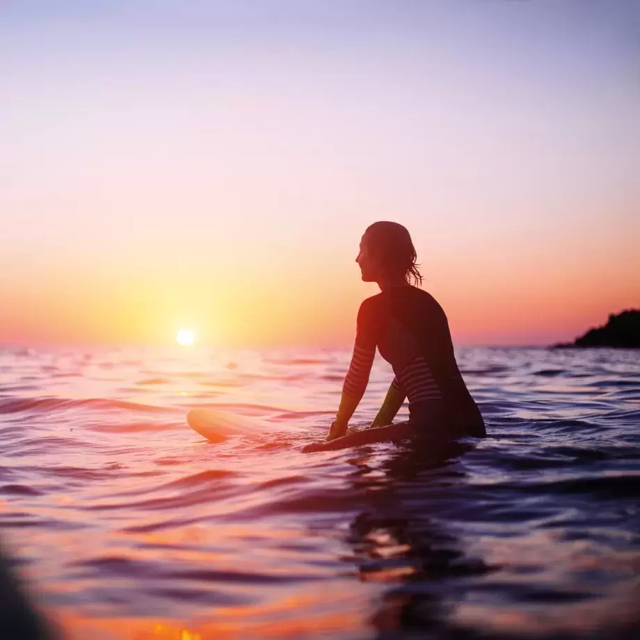 Silhouette of female surfer in the sea at sunset